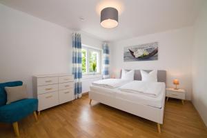 ein weißes Schlafzimmer mit einem Bett und einem blauen Stuhl in der Unterkunft Ferienwohnungen Rügen Findling Breege in Breege