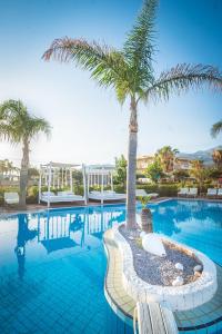 a swimming pool with a palm tree in the middle at Parthenis Hotel & Suites in Malia