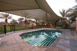 a swimming pool with an umbrella on a patio at Boudl Al Nakheel in Unayzah