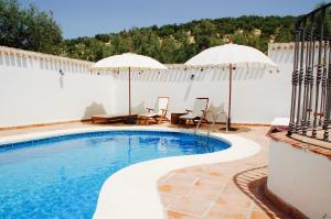 a swimming pool with two umbrellas and a patio with tables and chairs at Valle de Oro in Villanueva de Algaidas