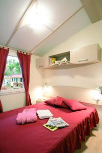 a bedroom with a red bed with red sheets and a window at New Camping Le Tamerici in Marina di Cecina