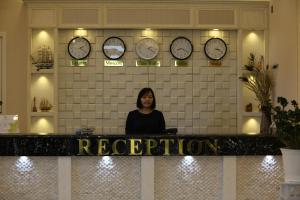 a woman standing behind a counter with clocks on the wall at Baigal Hotel in Ulaanbaatar