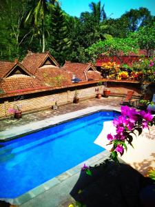 a swimming pool in front of a house with purple flowers at The Country House in Senggigi 