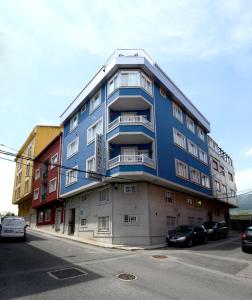 un edificio azul con coches estacionados frente a él en Hospedaxe A Vila, en Pobra do Caramiñal