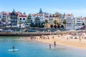 people on a beach with people on surfboards in the water at "Scandinavian" apartment in Cascais's old town in Cascais