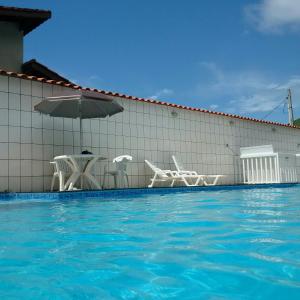 a swimming pool with chairs and an umbrella at Suítes Ubatuba Praia da Lagoinha in Ubatuba