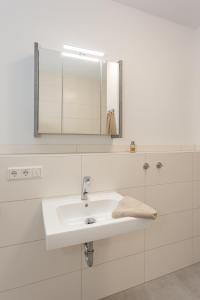 a white bathroom with a sink and a mirror at Komfort-Ferienwohnung Waterkant by Meer-Ferienwohnungen in Olpenitz +23 photos