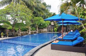 a swimming pool with blue chairs and umbrellas at Puri Dewa Bharata Hotel & Villas in Legian