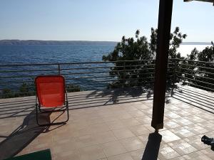 a red chair sitting on a patio overlooking the water at Apartman JURJEVIĆ in Barić Draga +23 photos