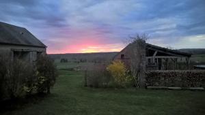an old barn in a field with a sunset in the background at Maison d'hôtes La Roulotte des 4 Saisons in Sazeray
