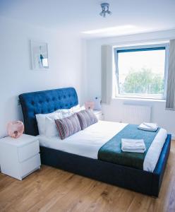 een slaapkamer met een bed met een blauw hoofdeinde en een raam bij RIVERSIDE 2 BED APARTMENT in North Woolwich