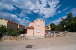 a pink house with a stone wall in a parking lot at Apartment Rose in Malinska