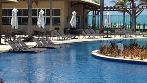 uma piscina com cadeiras e guarda-sóis num hotel em apartamento vista mar em Aquiraz