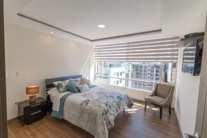 ein Schlafzimmer mit einem Bett, einem Fenster und einem Stuhl in der Unterkunft Suite de Lujo, Piso Alto, junto Parque Carolina in Quito