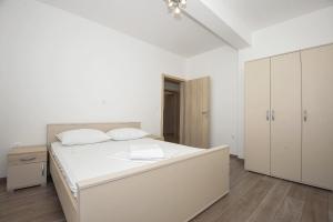 a white bedroom with a large white bed and cabinets at Apartmani Vrtlici Zdenka in Stara Novalja