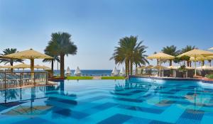 einen Pool mit Sonnenschirmen und dem Meer in der Unterkunft Bahi Ajman Palace Hotel in Ajman 