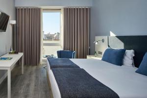 a hotel room with a bed and a desk and a window at Occidental Faro in Faro