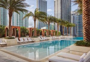 einen Pool mit Stühlen und Palmen in einer Stadt in der Unterkunft SLS LUX Brickell in Miami