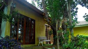 a yellow building with a bench next to a tree at Chalé Rancho Aratama in Jacareí
