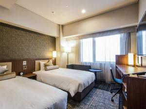 a hotel room with two beds and a desk at HOTEL UNIZO Osaka Shinsaibashi in Osaka