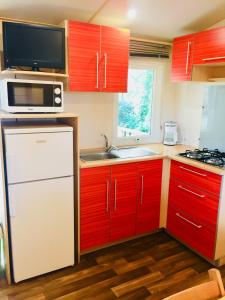 eine Küche mit roten Schränken, einer Mikrowelle und einer Spüle in der Unterkunft Camping Maureillas in Maureillas