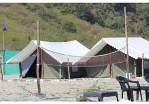 a tent on the beach with two chairs in front at The Junky Yard Camps in Rishīkesh