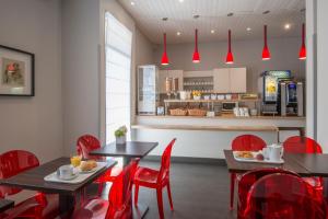 a dining room with red chairs and tables and a kitchen at Hôtel Amaryllis in Nice