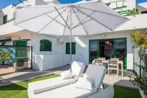 um pátio com um guarda-sol branco e cadeiras brancas em bungalow con gran terraza con vistas em Maspalomas