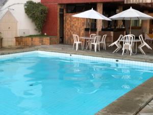 una piscina con sillas y sombrillas blancas, mesa y sillas en Flat Privativo Sol Victoria Marina, en Salvador