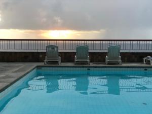 una piscina con 3 sillas y la puesta de sol en Flat Privativo Sol Victoria Marina, en Salvador