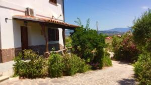 a white building with bushes next to a street at Agriturismo Su Meurreddu in Tratalias