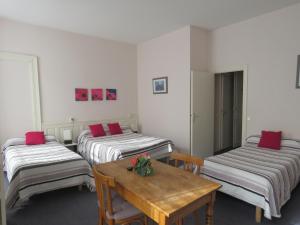 Habitación con 3 camas y mesa de madera. en Hotel Richelieu, en Eaux-Bonnes