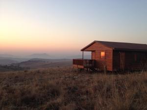 eine Hütte auf einem Feld mit Sonnenuntergang im Hintergrund in der Unterkunft Alto Log Cabin in Madeteleli