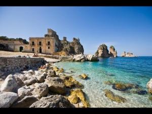 a beach with rocks and a building in the water at Villa Plaia in Castellammare del Golfo