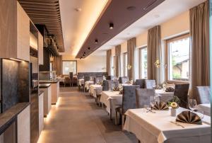 een restaurant met witte tafels, stoelen en ramen bij Hotel Winzerhof in Termeno