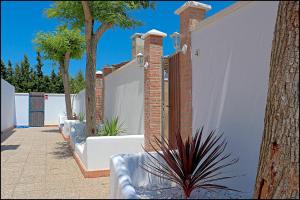 a white fence with trees and a plant next to it at Bungalow La Roa IV in Conil de la Frontera +25 photos