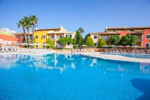 a large blue swimming pool with white chairs and buildings at Grupotel Playa Club in Son Xoriguer