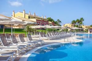 eine Reihe von Stühlen und Sonnenschirmen neben einem Pool in der Unterkunft Grupotel Playa Club in Son Xoriguer