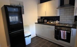 uma cozinha com armários brancos e um frigorífico preto em Buller House em Selby