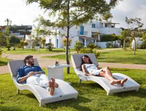 a man and woman sitting in lounge chairs in the grass at VOI Marsa Siclà Essentia in Sampieri