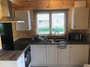 a kitchen with white cabinets and a sink and a window at Bacchus Hotel Log Cabins in Sutton on Sea