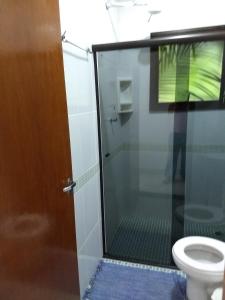 La salle de bains est pourvue d'une porte de douche en verre et de toilettes. dans l'établissement RC Sol de Boiçucanga - Suite, à Boicucanga