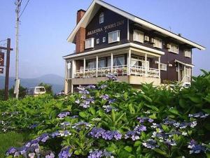 une grande maison avec des fleurs devant elle dans l'établissement Akakura Yours Inn, à Myōkō