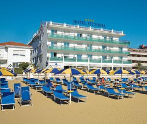 ein paar Stühle und Sonnenschirme am Strand in der Unterkunft Hotel Vittoria in Lignano Sabbiadoro