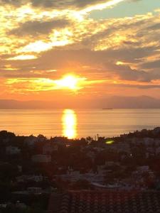 a sunset over a city with the sun setting over the water at Modern Apartment with sea view in Saronida in Anavissos