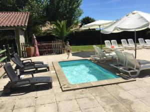 a swimming pool with chairs and an umbrella and a boy walking by it at la ferme des 4 chenes in Urt