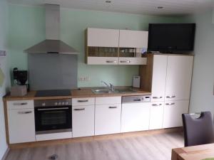 a kitchen with white cabinets and a tv on the wall at Ferienwohnung Moselblick in Ediger-Eller