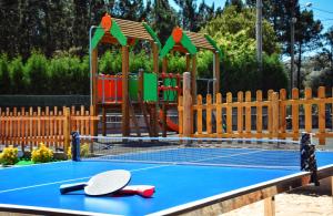 a tennis court with two tennis rackets and a playground at Camping Preguntoiro in Sanxenxo