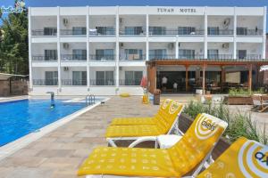 a hotel with yellow lounge chairs next to a swimming pool at Tunan Motel in Ayvalık