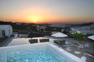 een zwembad met stoelen en parasols en de zonsondergang bij Nova Luxury Suites in Pirgos